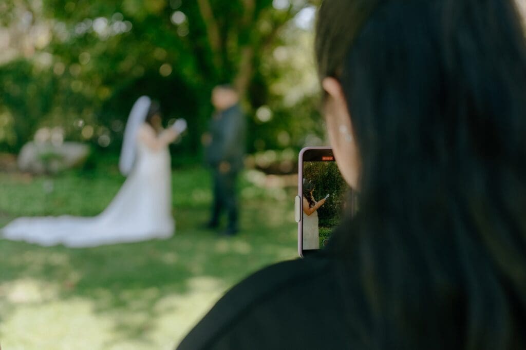 Wedding content creator filming bride and groom reading private vows behind the scene with iphone