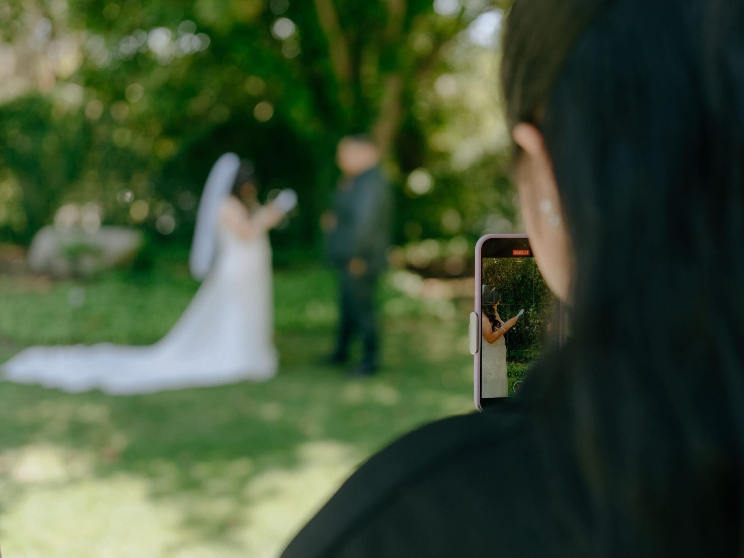Wedding content creator filming bride and groom reading private vows behind the scene with iphone